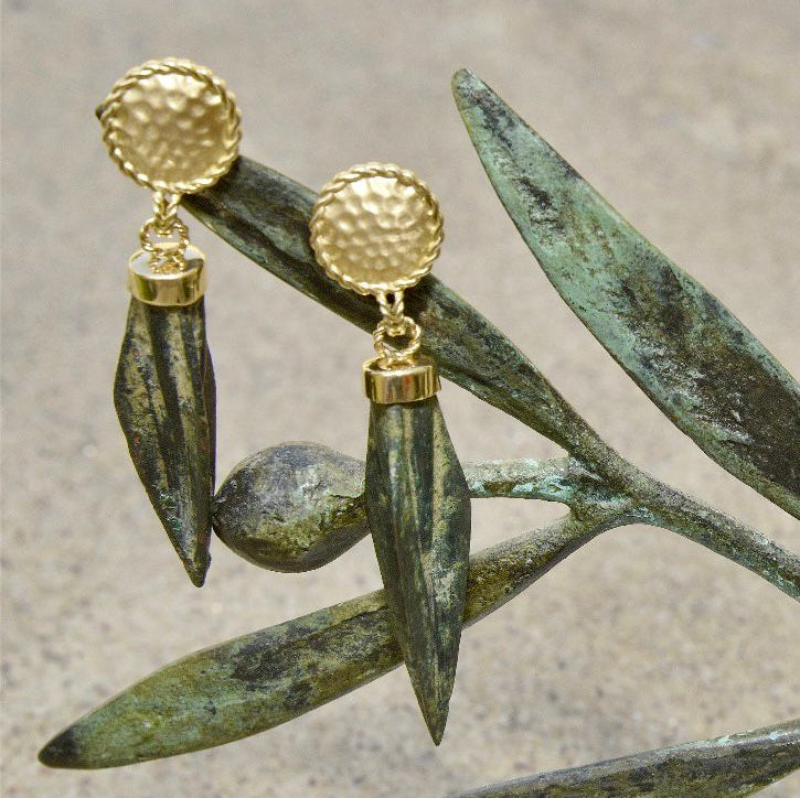 Gold earrings with green leaves on a textured surface