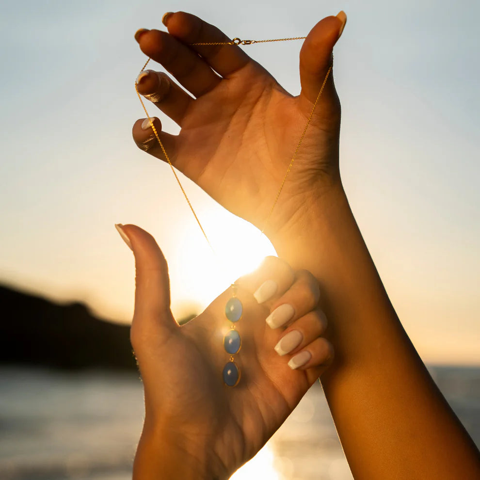 Hand holding a necklace with a sunset in the background