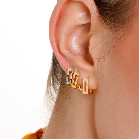 Gold hoop earrings with blue gemstones worn by a person on a white background
