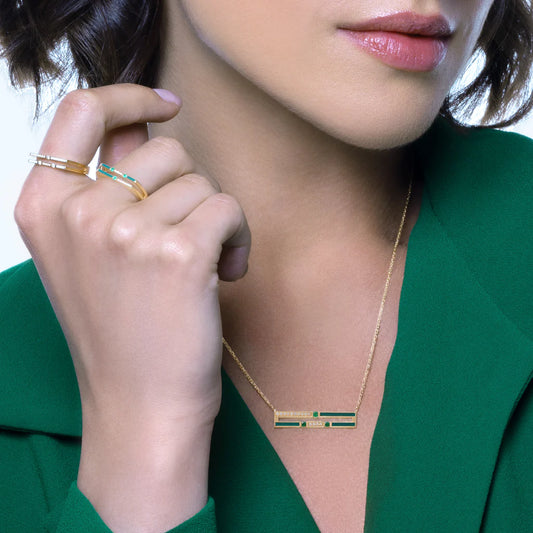 Close-up of a person wearing a gold necklace with a green pendant, hand resting on face.