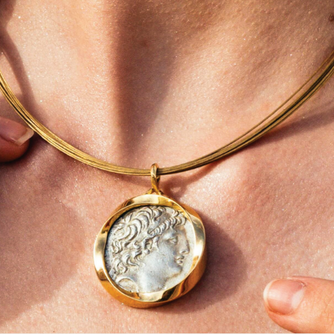 Gold necklace with a pendant featuring a classical design on a person's neck.