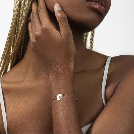 Woman wearing a gold bracelet on her wrist with a neutral background