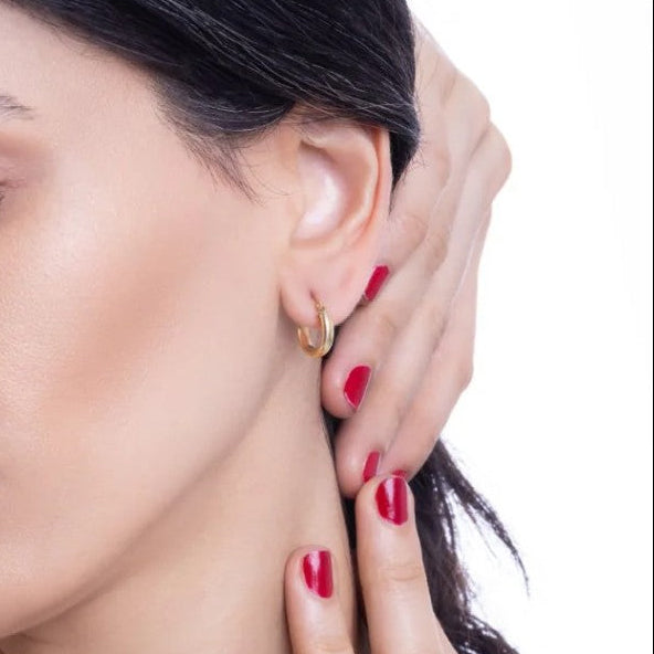 Close-up of a woman wearing a gold hoop earring with a neutral background