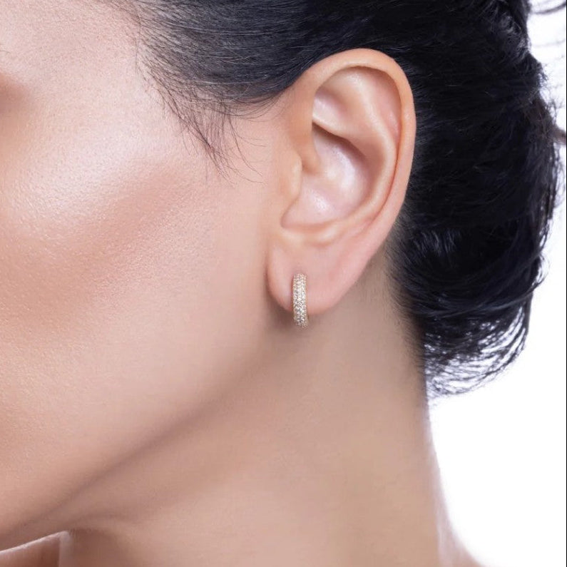 Close-up of an ear wearing a gold hoop earring with a blurred background