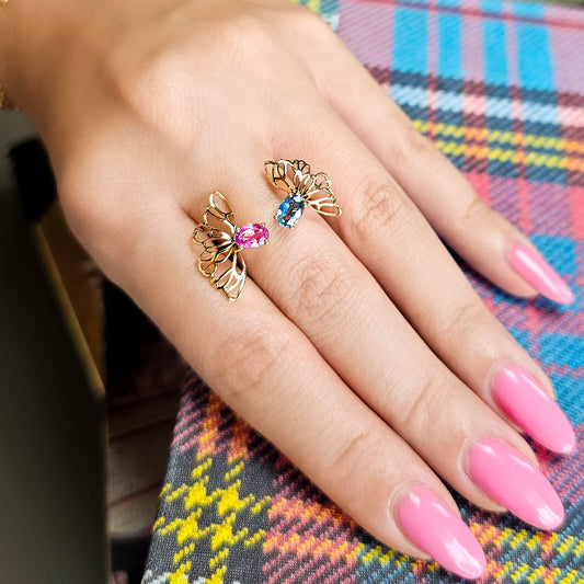 Hand wearing two gold butterfly rings with gemstones on a colorful plaid fabric background