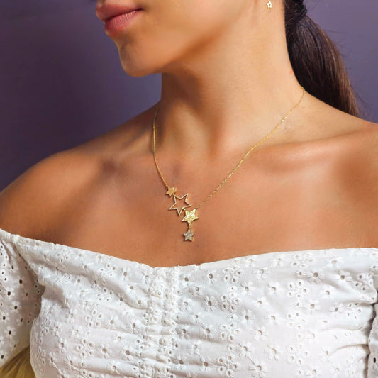 Woman wearing a gold necklace with star pendants against a purple background