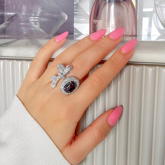 Hand wearing a ring with pink nail polish on a neutral background