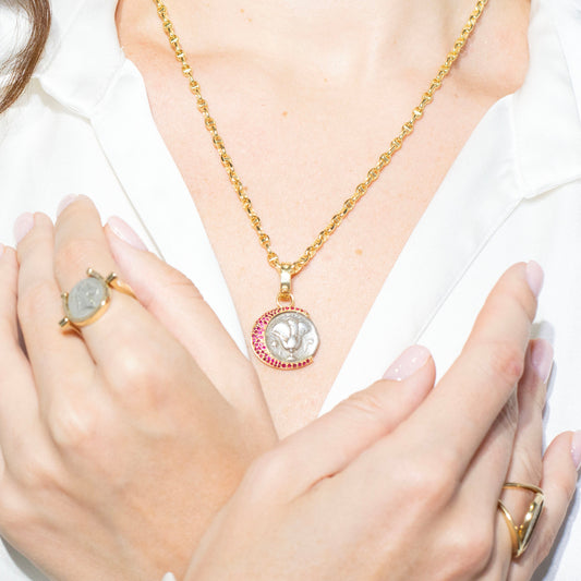 Person wearing gold jewelry including a necklace, ring, and bracelet on a plain background