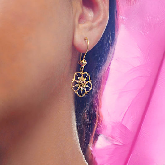 Gold floral earring worn by a person with a pink garment in the background