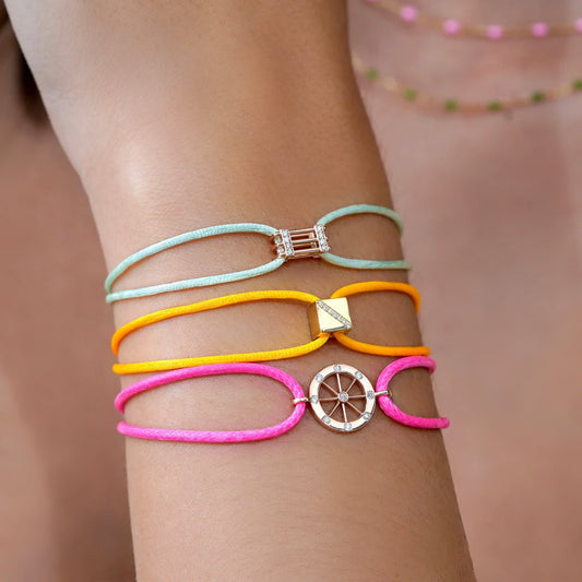 Close-up of a wrist wearing three colorful bracelets with decorative elements on a blurred background.
