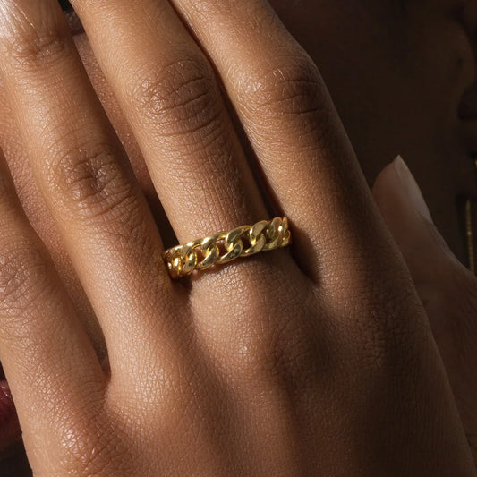 Gold chain ring on a person's finger with a warm, soft focus background