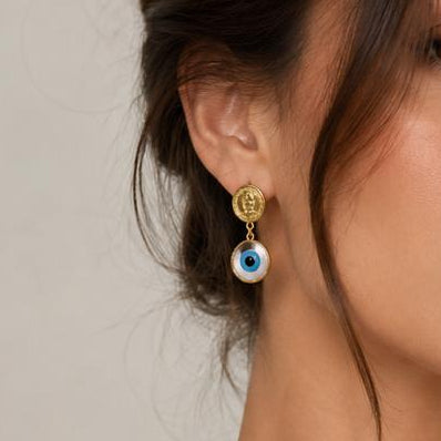 Woman wearing a gold necklace with blue eye pendants on a neutral background