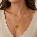 Woman wearing gold heart-shaped necklace and earrings against a neutral background