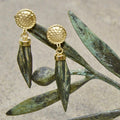 Gold earrings with green leaves on a textured surface