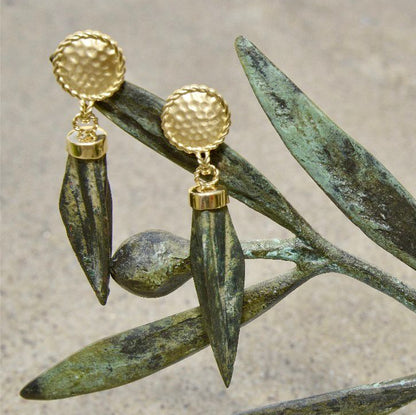 Gold earrings with green leaves on a textured surface