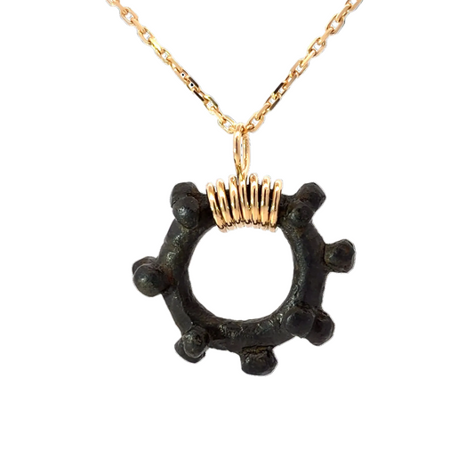 Black pendant with gold accents on a gold chain against a white background