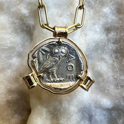Gold necklace with a silver coin pendant featuring an owl on a marble surface