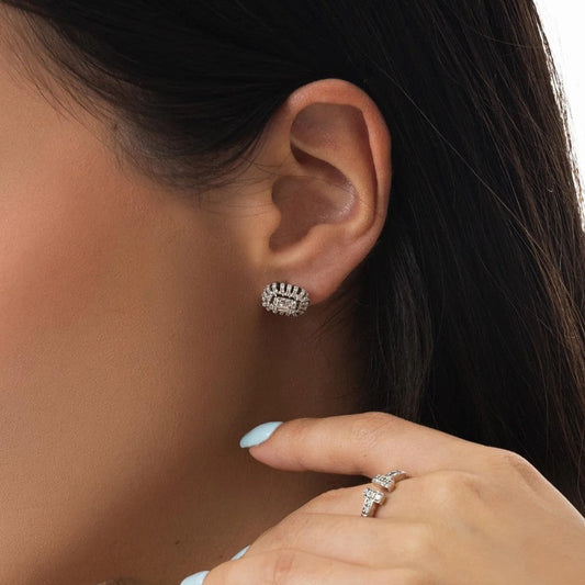 Close-up of an ear wearing a diamond earring with a hand holding a ring.