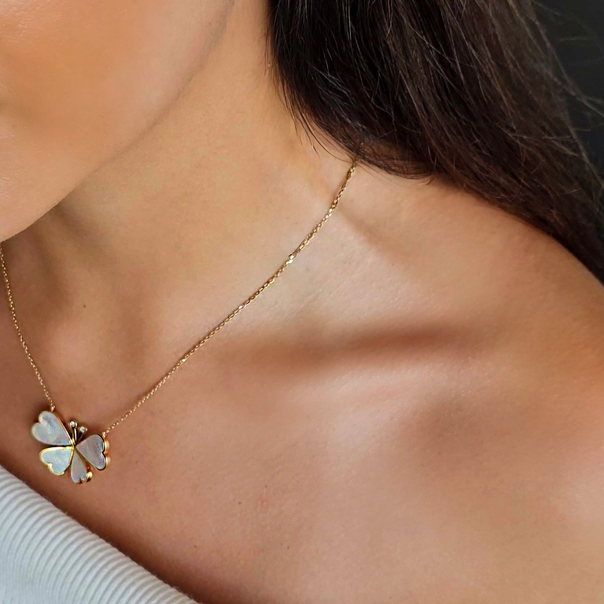 Gold necklace with a clover-shaped pendant on a person's neck