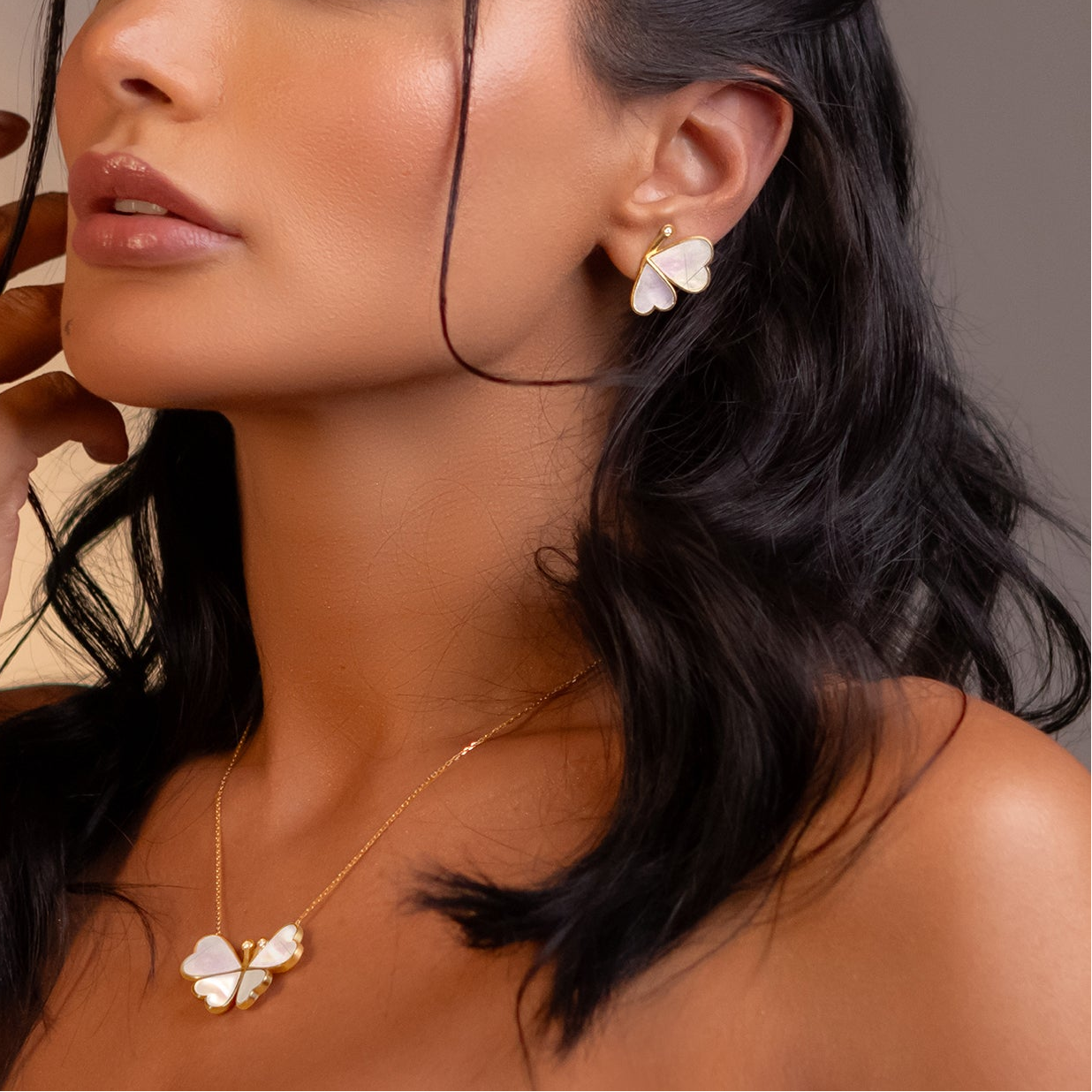 Close-up of a woman wearing floral earrings and a necklace against a neutral background