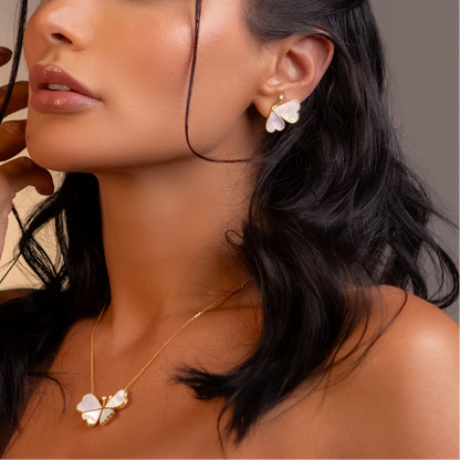 Close-up of a woman wearing floral earrings and a necklace against a neutral background