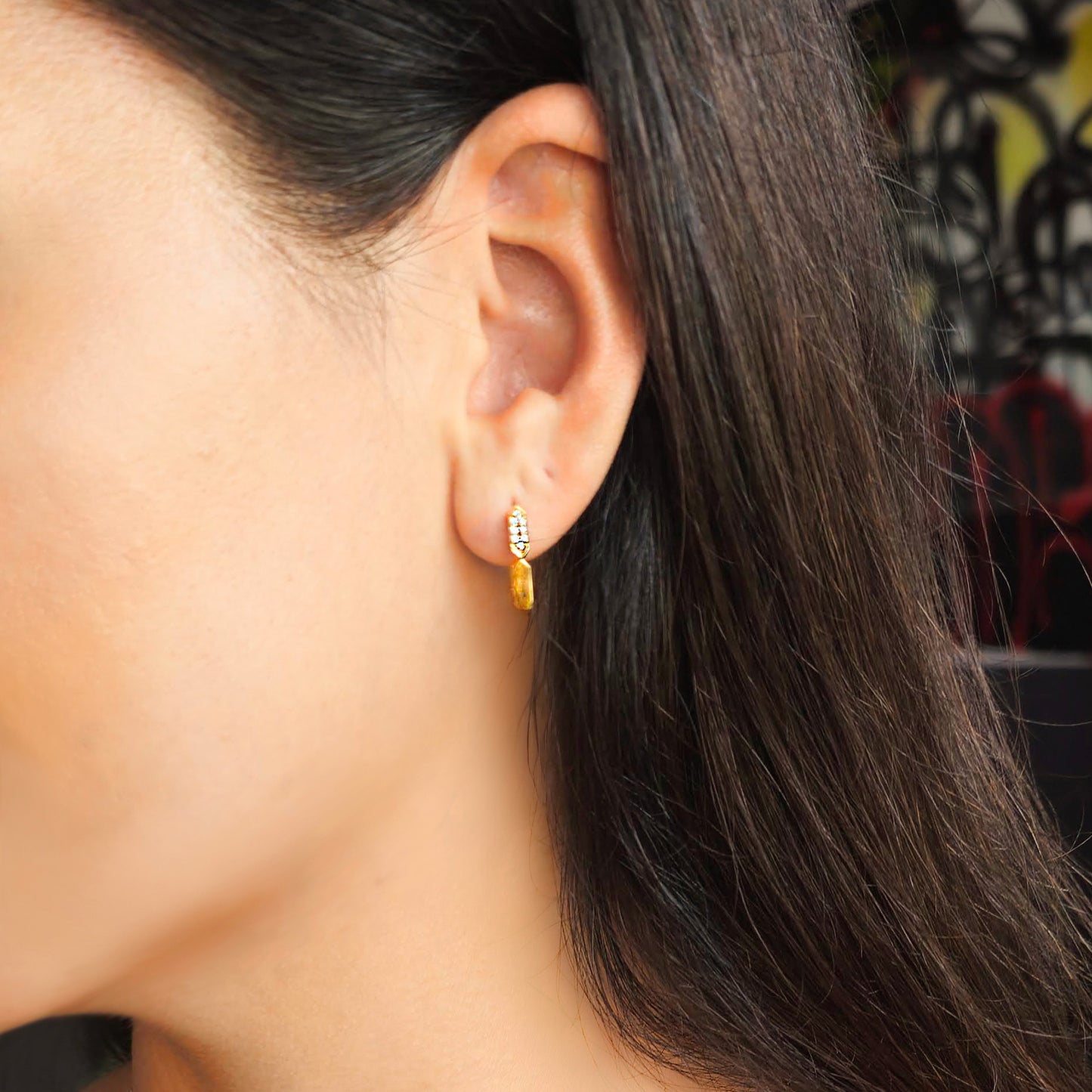 Close-up of an ear wearing a gold earring with a blurred background