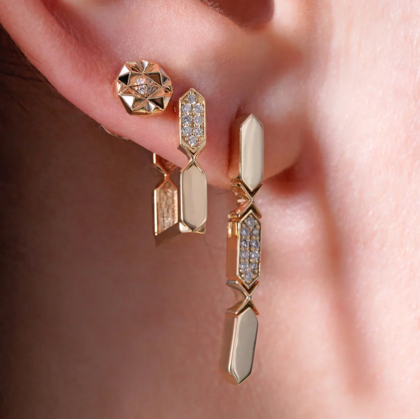 Gold earrings with geometric designs worn on an ear