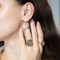 Close-up of a woman wearing gold earrings and rings with a neutral background