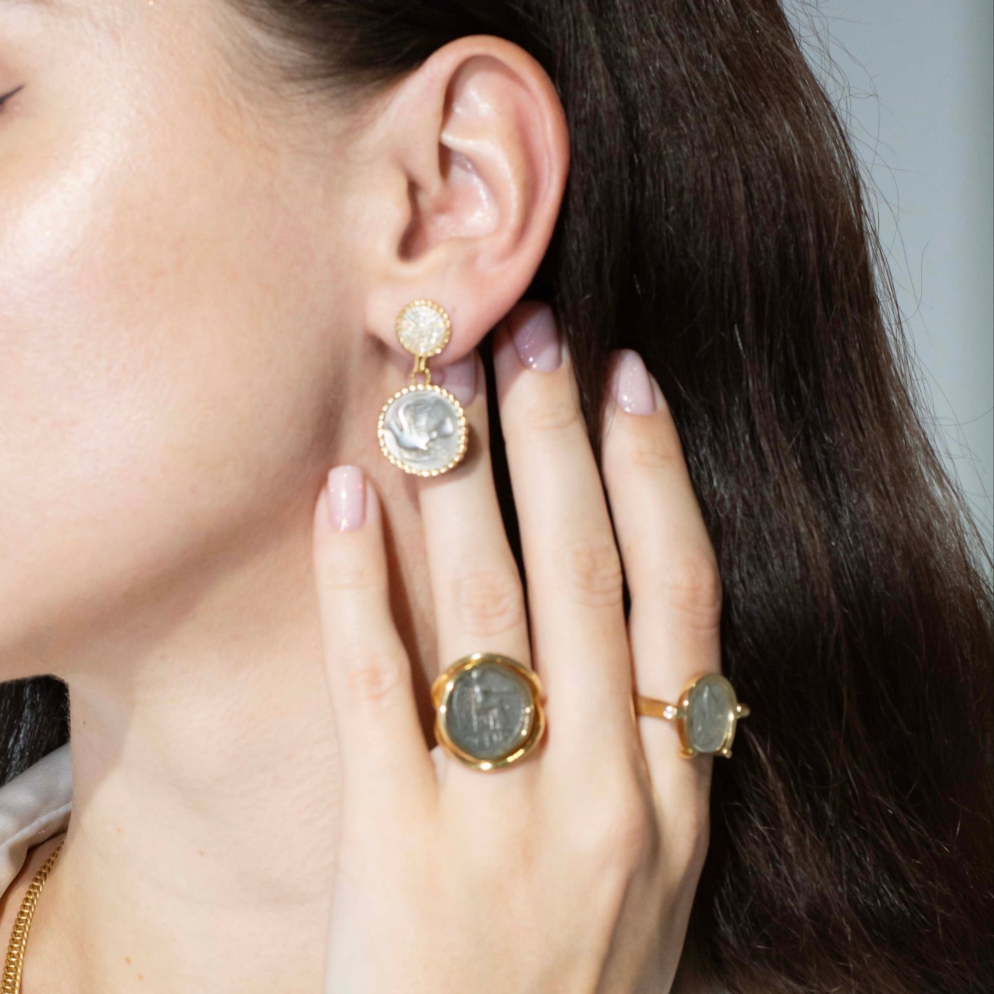Close-up of a woman wearing gold earrings and rings with a neutral background