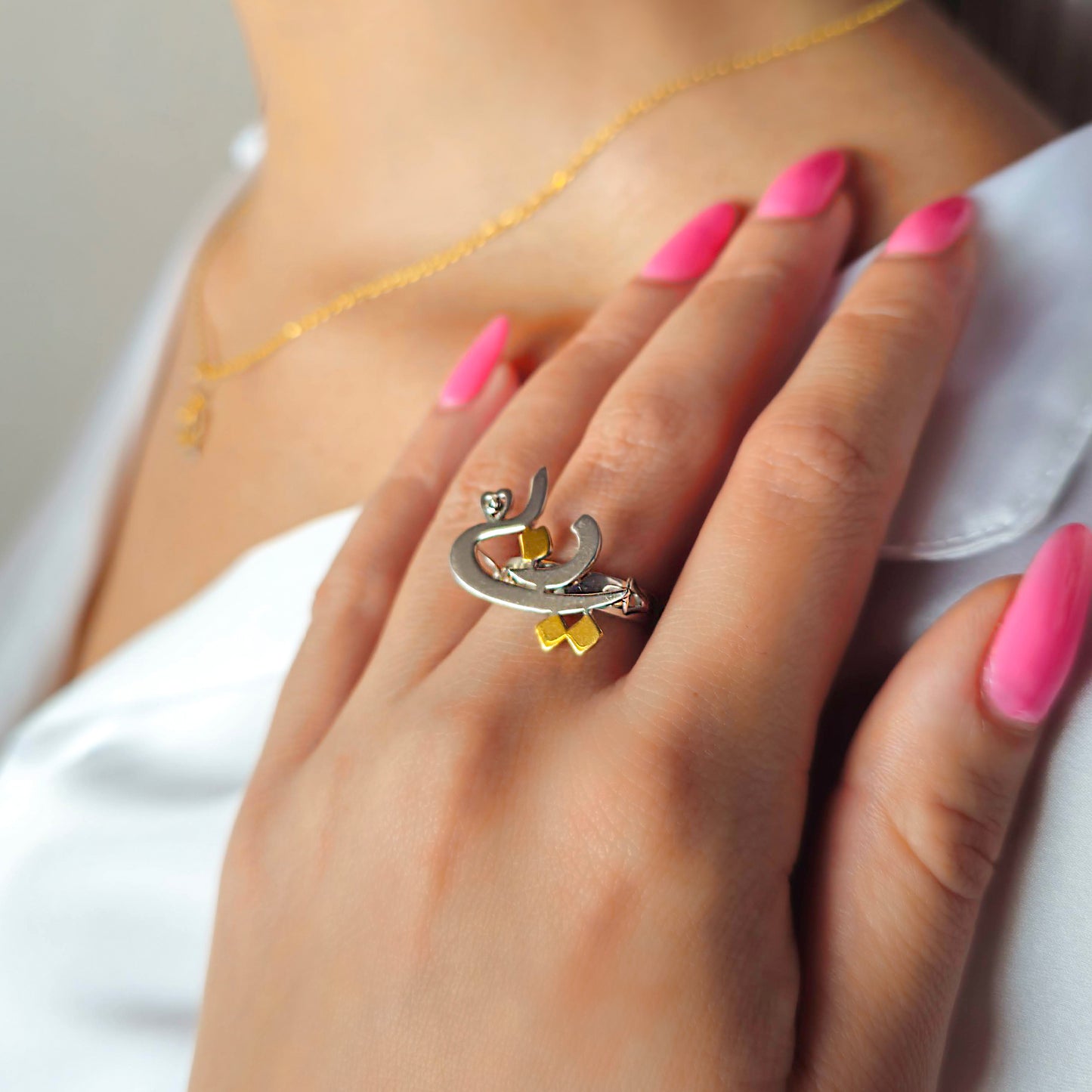 Close-up of a hand wearing a unique ring with pink nail polish on a neutral background