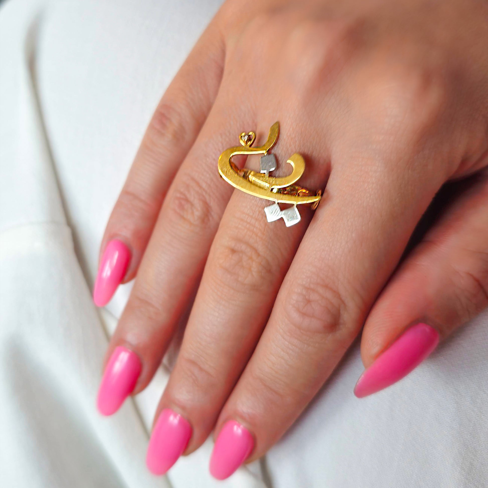 Gold ring with a unique design on a hand with pink nails against a white background