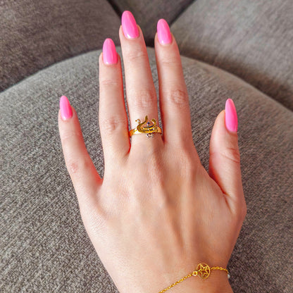 Hand wearing a gold ring with pink nail polish on a brown surface