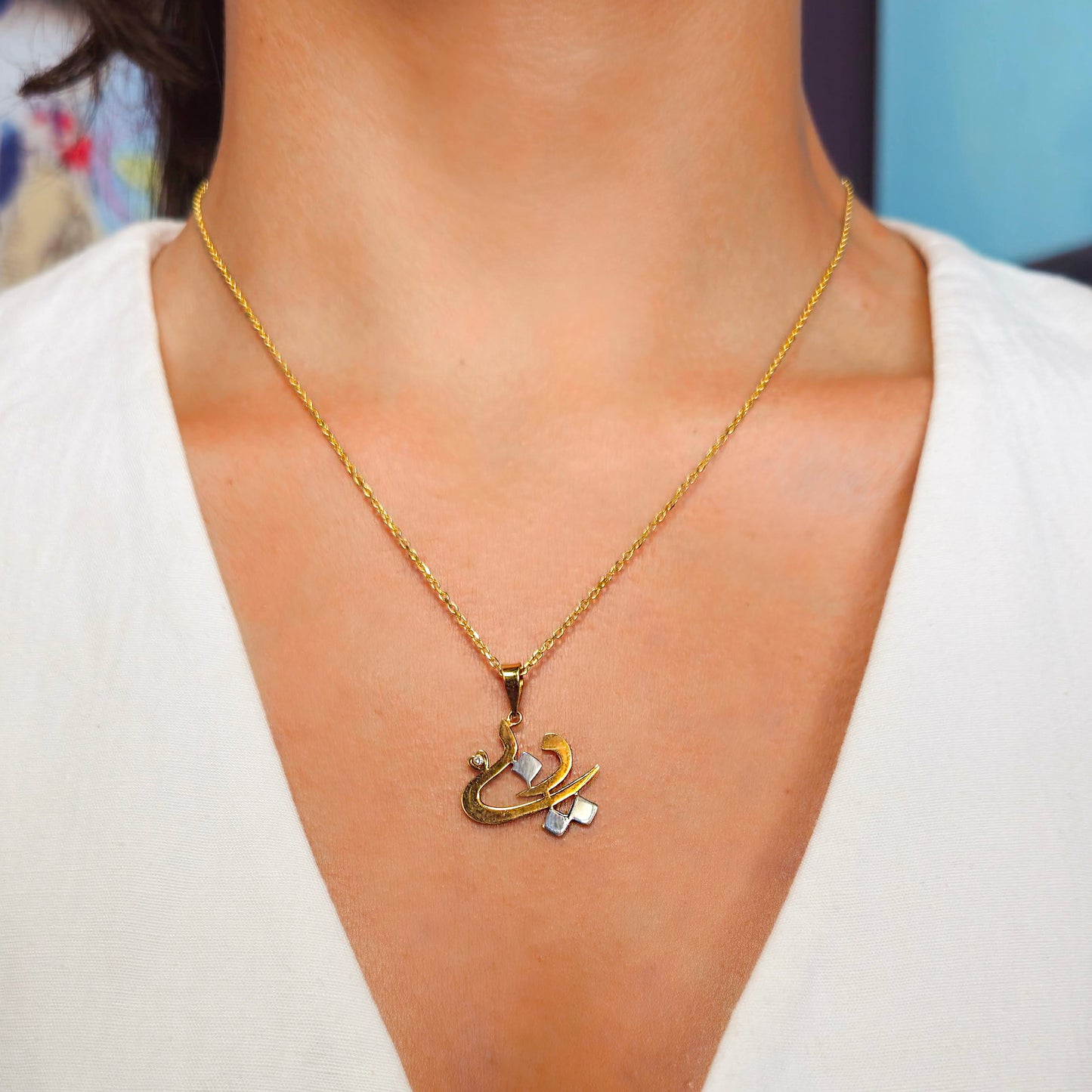 Gold necklace with a unique pendant worn by a person against a neutral background
