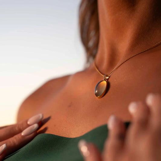 Close-up of a person wearing a gold necklace with a pendant, with a blurred background.