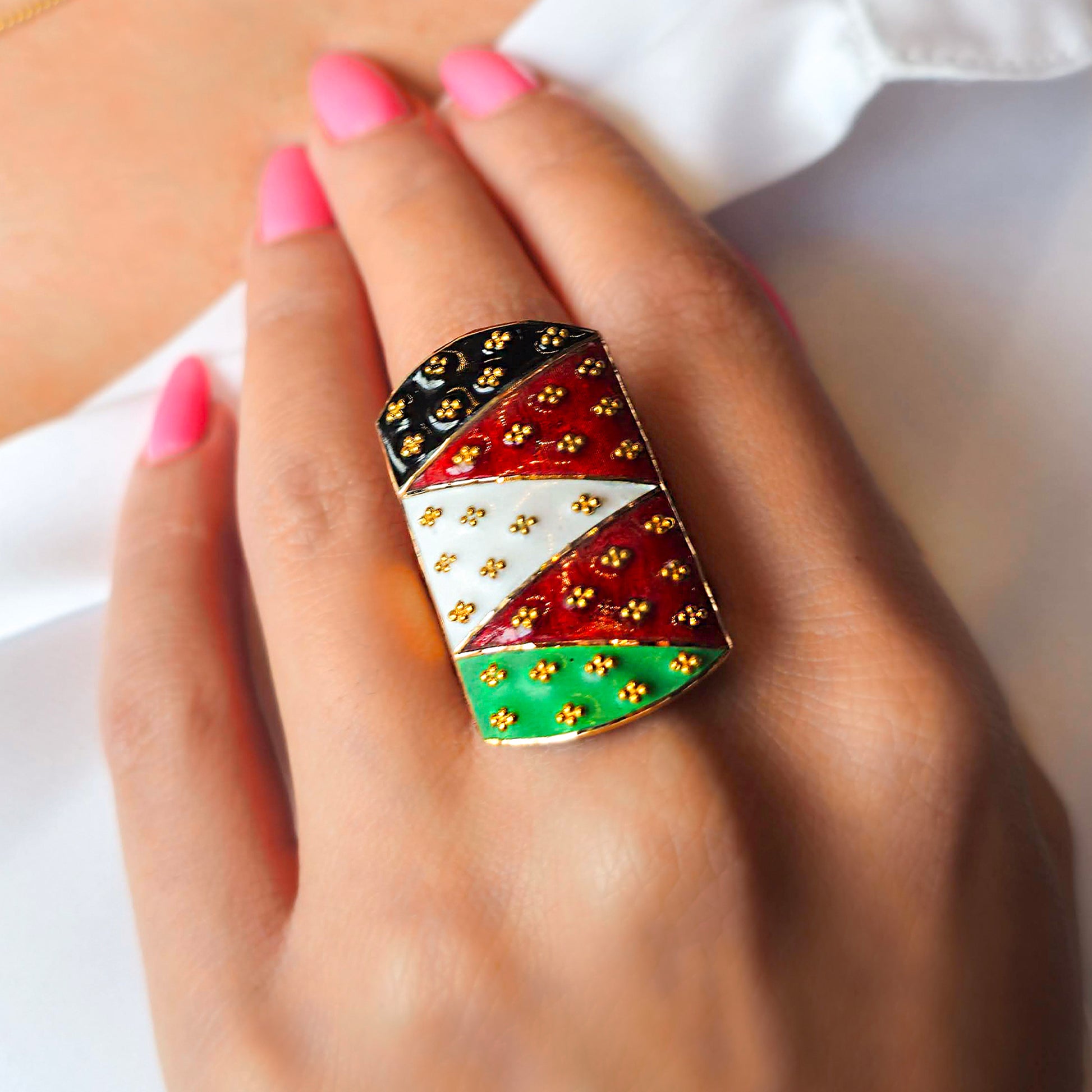 Colorful patterned ring on a hand with pink nail polish against a white background