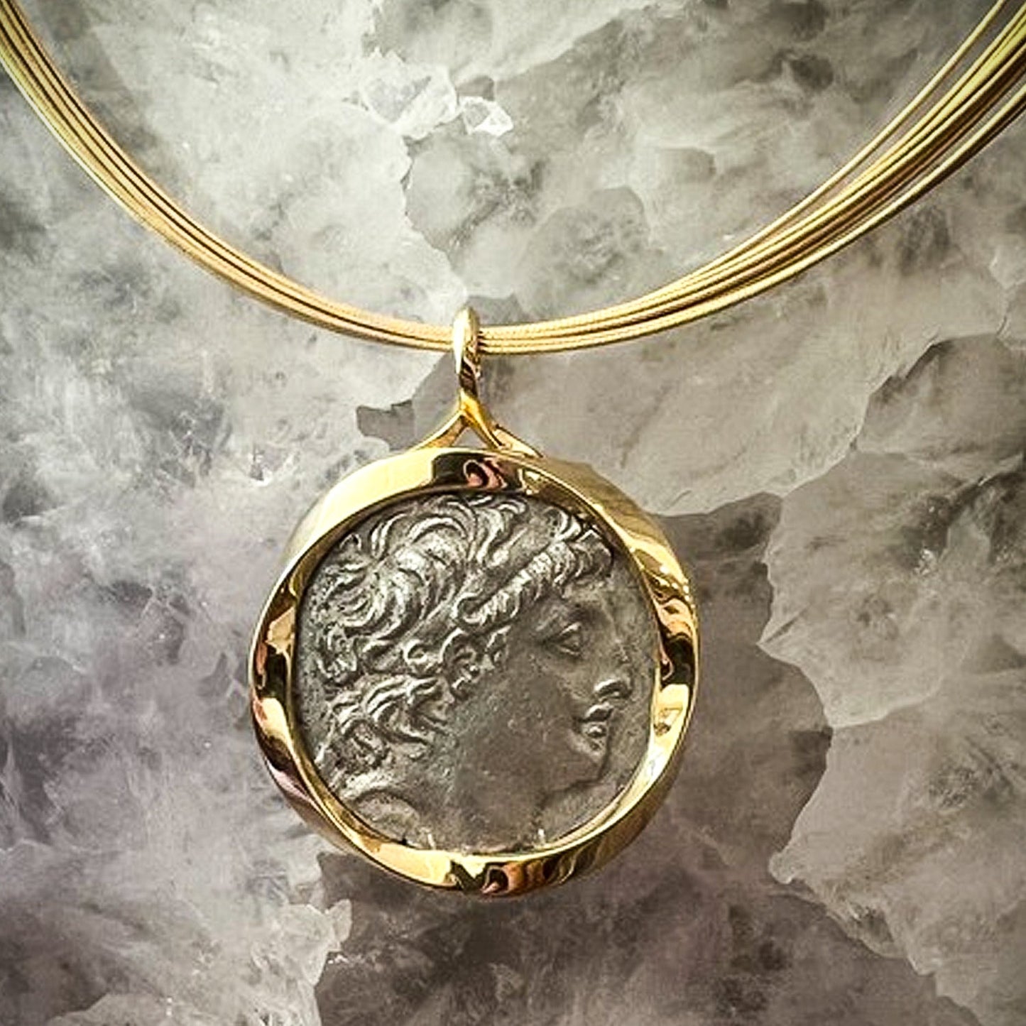Gold necklace with a pendant featuring an engraved face on a textured gray background