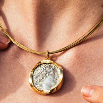 Gold necklace with a pendant featuring a classical design on a person's neck.
