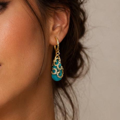 Woman wearing gold necklace and earrings with turquoise accents against a neutral background