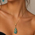 Woman wearing gold necklace and earrings with turquoise accents against a neutral background