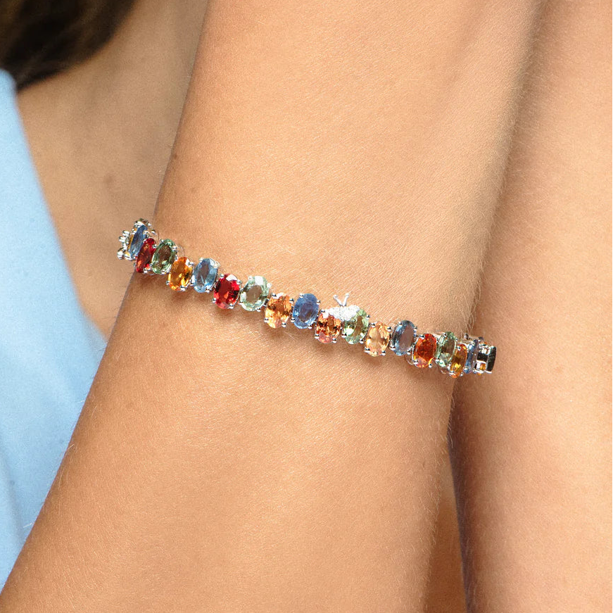 Multicolored gemstone bracelet on a person's wrist with a light blue sleeve.