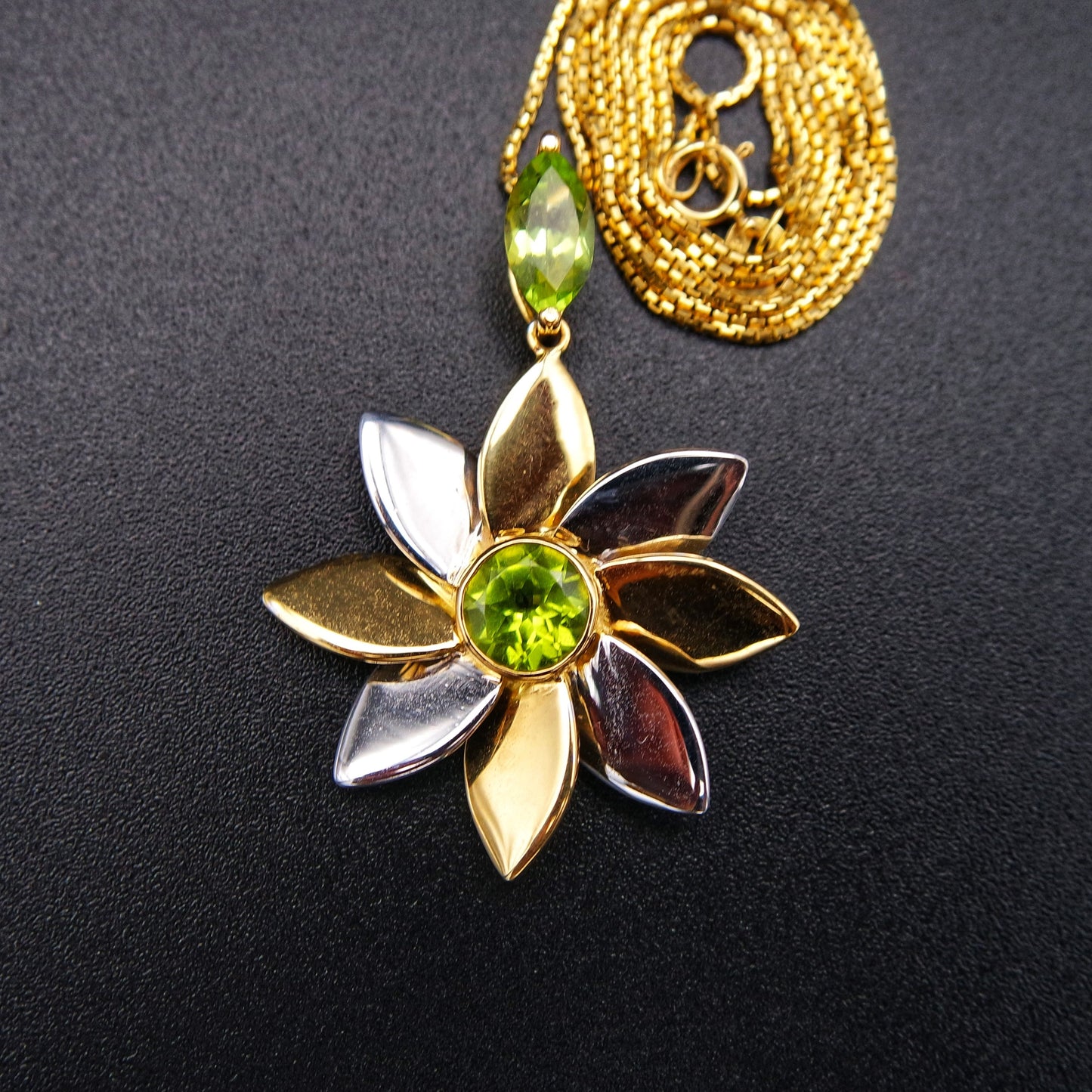 Gold flower-shaped pendant with green gemstones on a black background