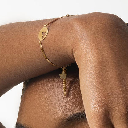 Gold bracelet with heart-shaped pendant on a person's wrist against a white background