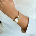Gold bracelet with a white flower design on a wrist against a white background