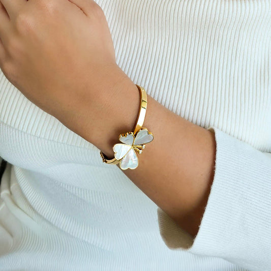 Gold bracelet with a white flower design on a wrist against a white background