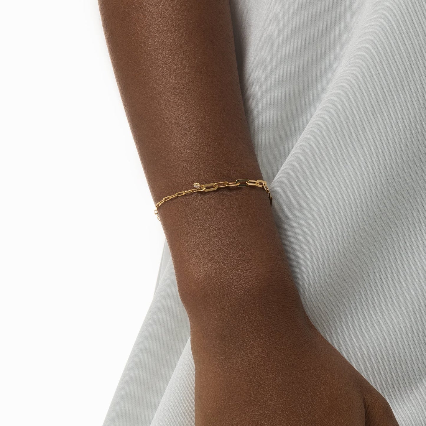 Gold bracelet on a wrist with a white fabric background