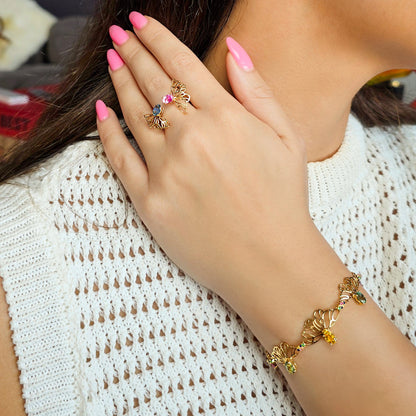 Close-up of a hand wearing a gold ring and bracelet with pink nail polish, against a white textured background.