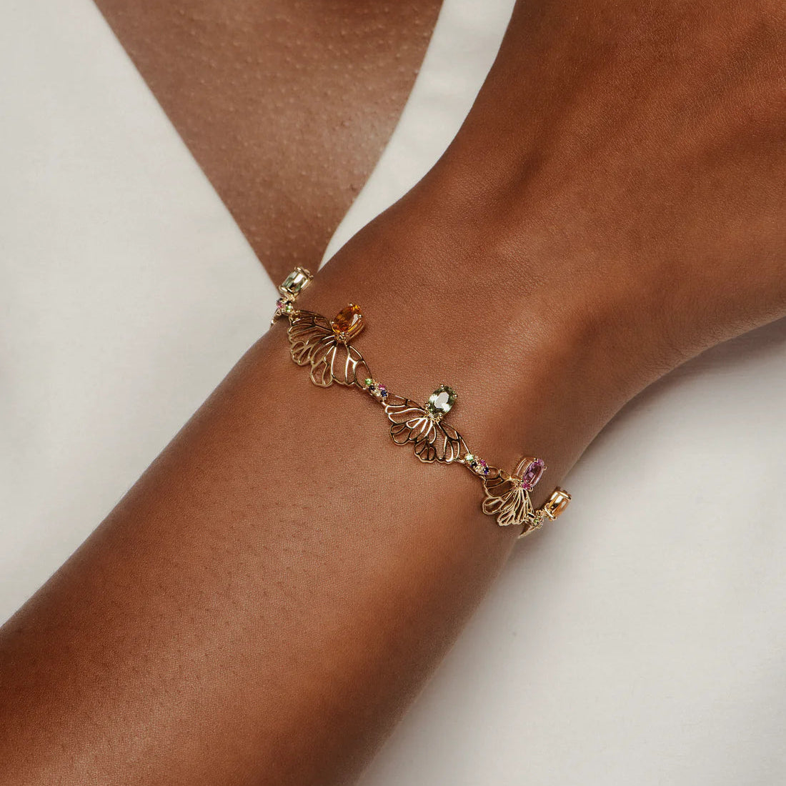 Gold bracelet with gemstones on a wrist against a neutral background