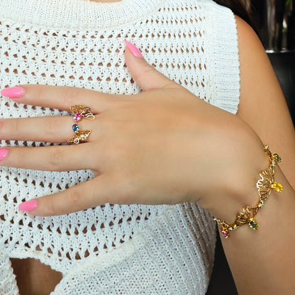 Hand wearing a gold ring and bracelet with colorful stones on a white lace background