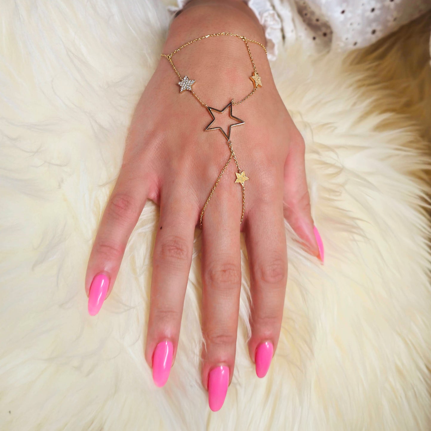 Hand wearing a gold star-shaped bracelet on a fluffy white surface
