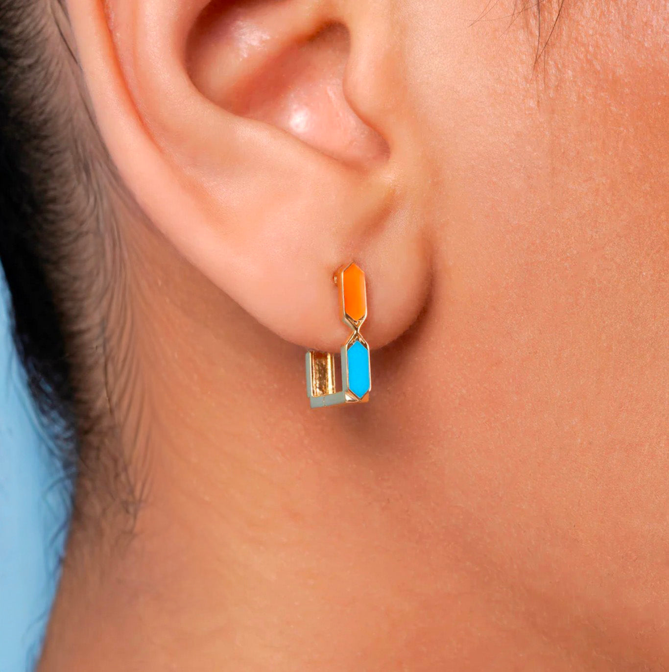 Close-up of an ear wearing a colorful earring against a neutral background